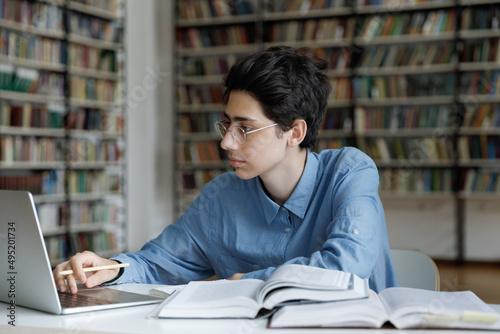 Student guy works on summary or essay, busy in exams preparations sit at table with books use laptop studying in university library. Young gen use modern tech to gain new knowledge, education concept