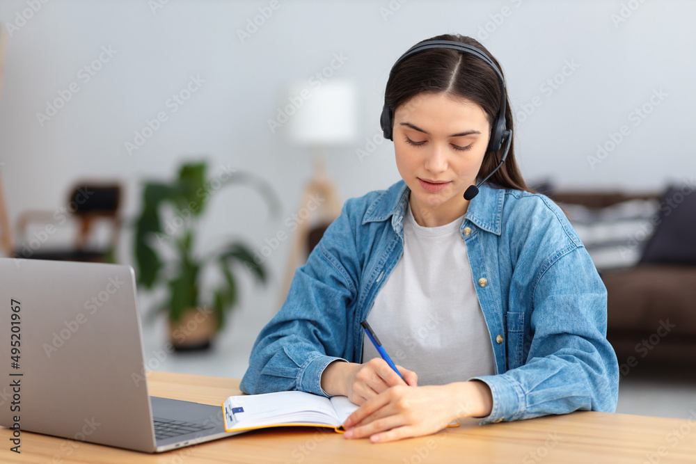 Young smiling freelancer in headset using laptop computer working online from home or modern office. Successful caucasian young female student studying, distance learning, education