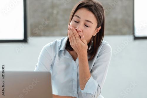 Close up portrait of tired caucasian woman office worker yawns covers mouth sitting at the workplace in the office or at home. Chronic sleep deprivation, overwork concept photo