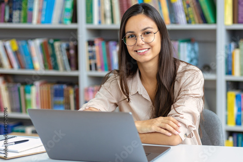 Distance learning, online education. Portrait of smiling caucasian young female student sitting in the library at the university. Freelancer working in co-working or modern office, smiling