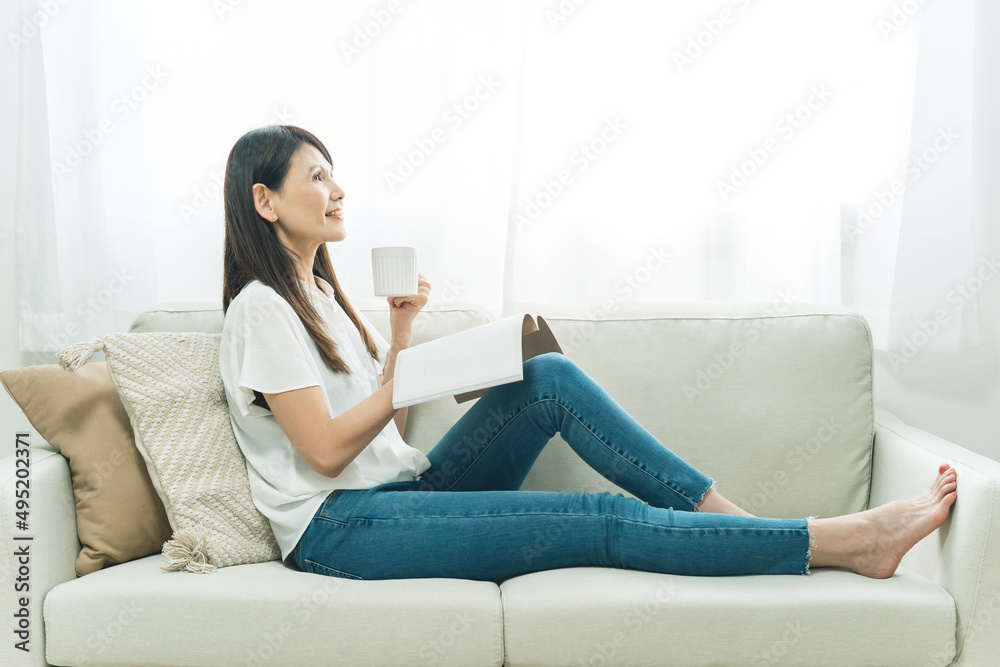 ソファに座る中高年女性（飲み物、読書）
