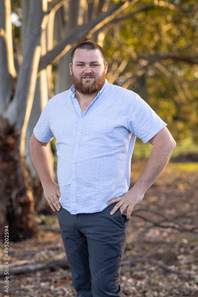 bearded man with hands on hips standing outdoors with trees in background bearded man with hands on hips standing outdoors with trees in background
