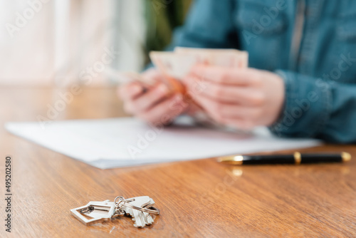 Close up of key with keychain lies on the table. Defocused person's hands counting money at the background. Concept of purchase of real estate and mortgage