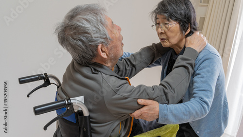 車イスから高齢の夫を立ち上がらせようとする高齢の妻