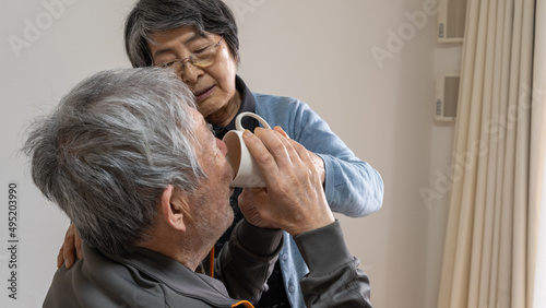 高齢の男性がコップでジュースを飲むのを手助けする高齢の女性