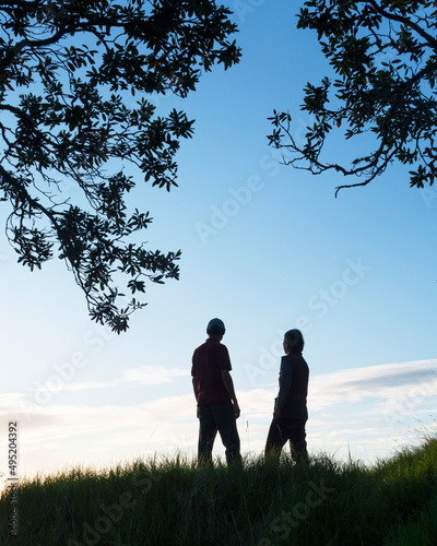 Silhouette couple standing on the hilltop looking at the sunrise, vertical format. © Janice