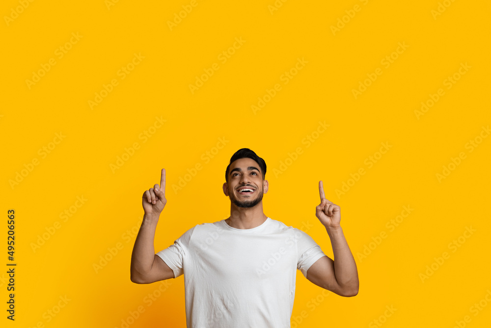 Cheerful arab guy pointing up at copy space for advertisement Cheerful arab guy pointing up at copy space for advertisement