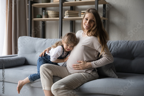 Joyful adorable little kid putting ear on belly of young pregnant mother, listening to future baby. Happy bonding family waiting for childbirth, feeling unconditional life, having fun together at home
