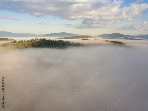 Flight over fog in Ukrainian Carpathians in summer. Mountains on the horizon. A thick layer of fog covers the mountains with a continuous carpet. Aerial drone view.