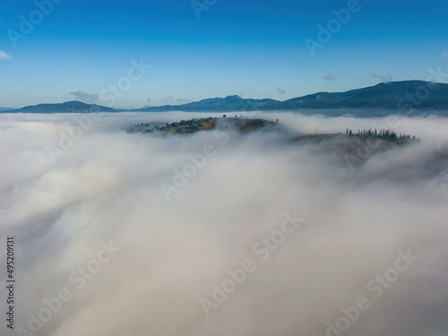 Sunny morning in the foggy Carpathians. A thick layer of fog covers the mountains. Aerial drone view. © Sergey