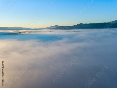 Flight over fog in Ukrainian Carpathians in summer. Mountains on the horizon. A thick layer of fog covers the mountains with a continuous carpet. Aerial drone view. © Sergey