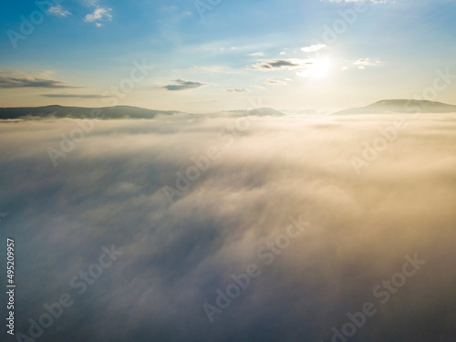 Flight over fog in Ukrainian Carpathians in summer. Mountains on the horizon. A thick layer of fog covers the mountains with a continuous carpet. Aerial drone view.