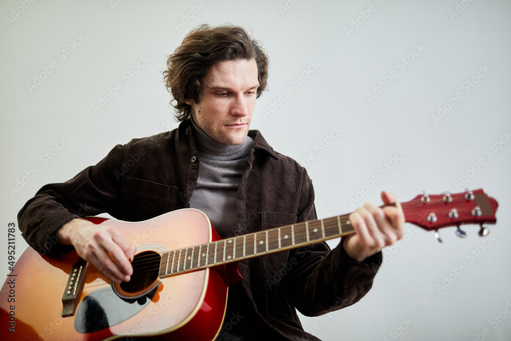 Obraz premium Young man enjoying his play on guitar sitting against the grey background