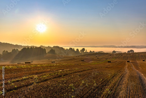 Rural landscape. Colorful sunrise in foggy countryside over agricultural field with harvested wheat