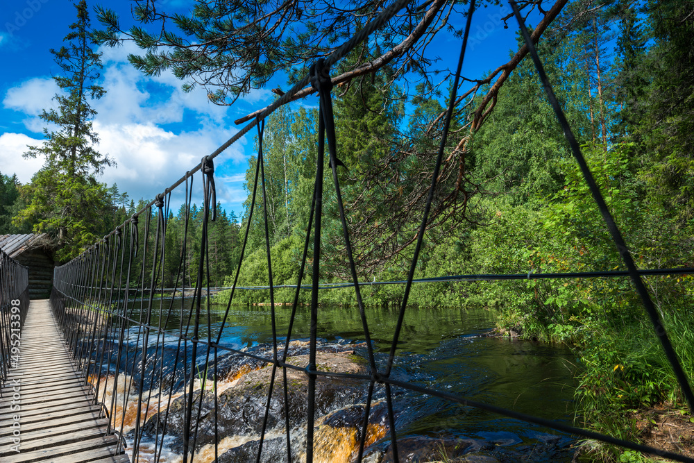 Fototapeta premium Suspension bridge and wooden house on Ruskeala waterfalls in Karelia, Russia