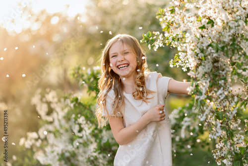 Portrait of laughing girl under falling petals of cherry blossom flowers in spring.