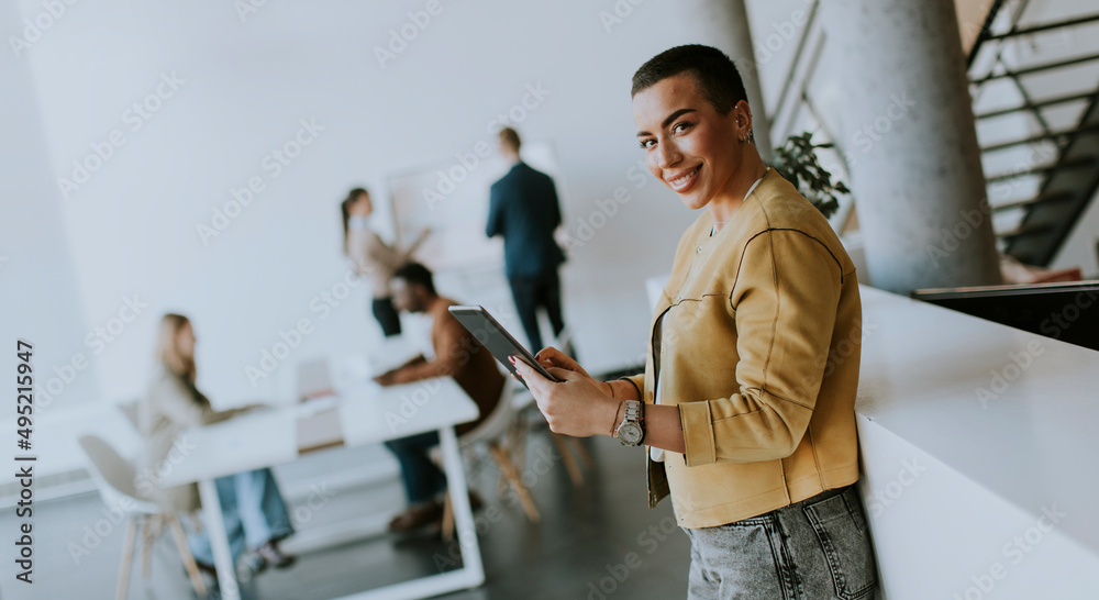 Young short hair business woman standing in office and using digital tablet in front of her team