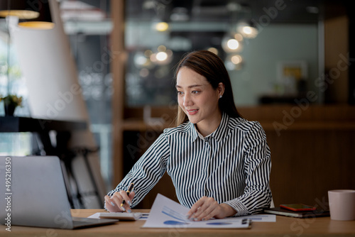 A beautiful Asian businesswoman sitting in her private office, she is checking company financial documents, she is a female executive of a startup company. Concept of financial management.