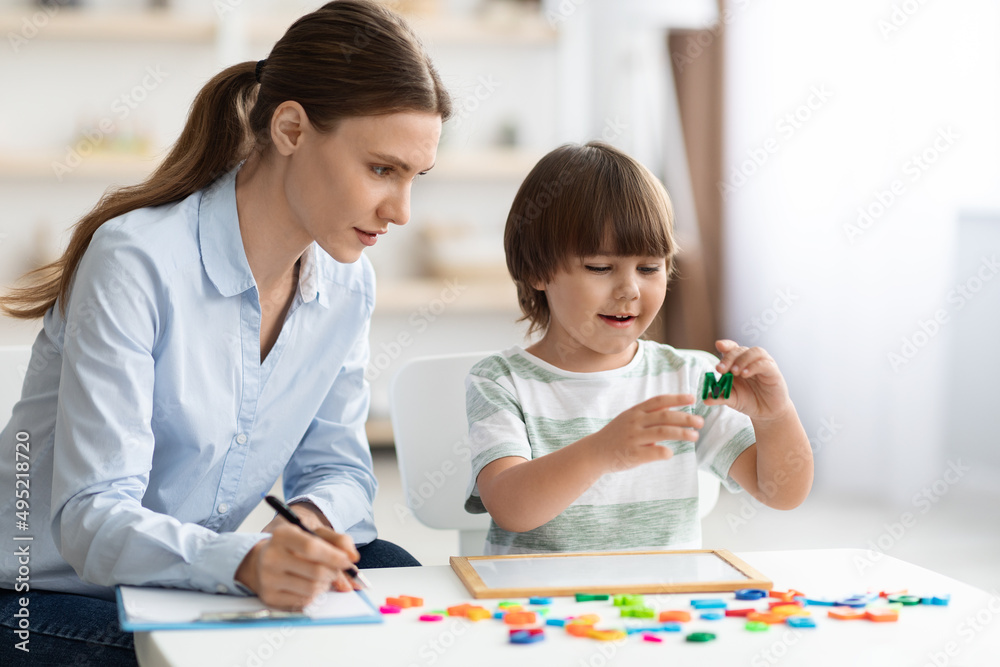 Cute little clever boy holding letter M, exercising with teacher at classroom, free space Cute little clever boy holding letter M, exercising with teacher at classroom, free space