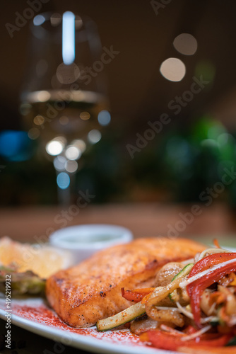 closeup of roasted salmon steak with wok vegetable and sauce on white plate