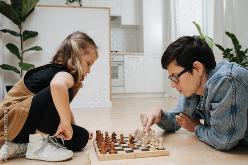 Competitive chess match between dad and his child daughter. Both excited and having fun. Side view. On the kitchen floor.