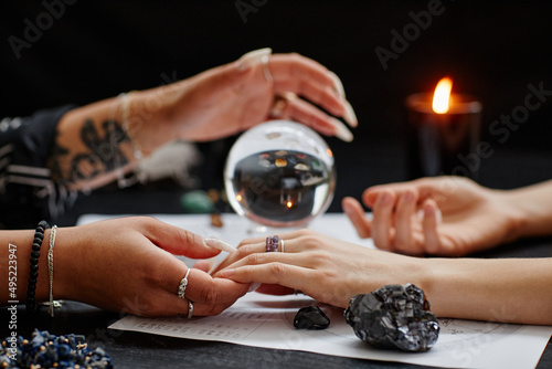 Close up of fortune teller holding hand of young woman during spiritual seance with crystal ball