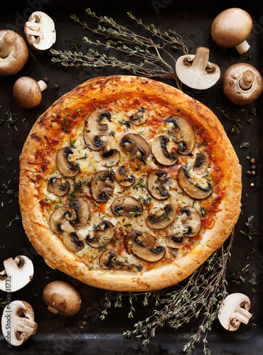 Mushroom pizza with the addition of sliced brown mushrooms, champignons and herbs on a black background, top view