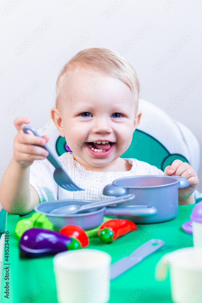 a small child plays children's dishes with vegetables, sitting at the table a small child plays children's dishes with vegetables, sitting at the table
