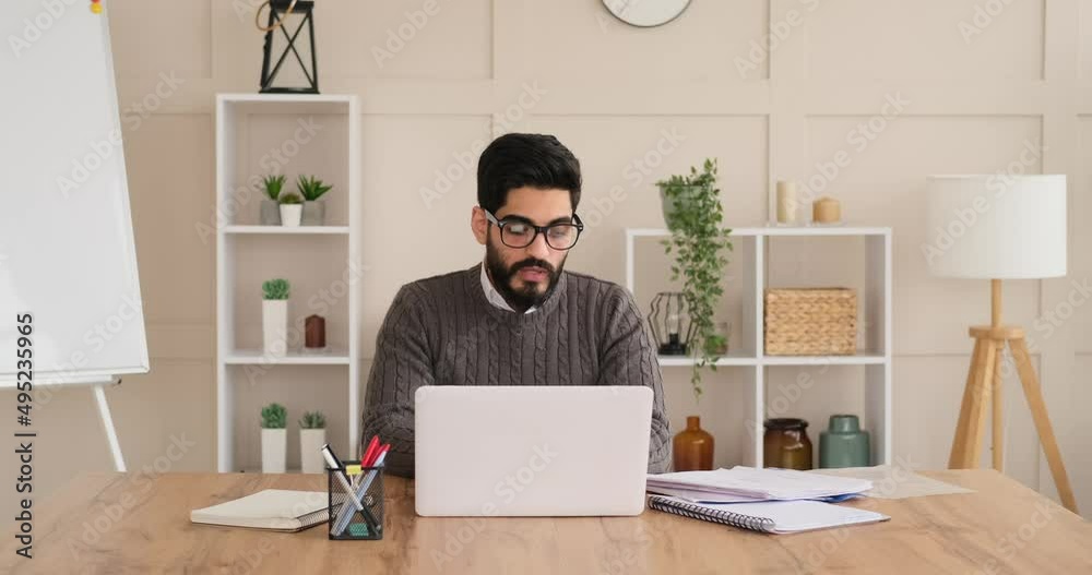 Businessman reading document while video conferencing on laptop at office Businessman reading document while video conferencing on laptop at office