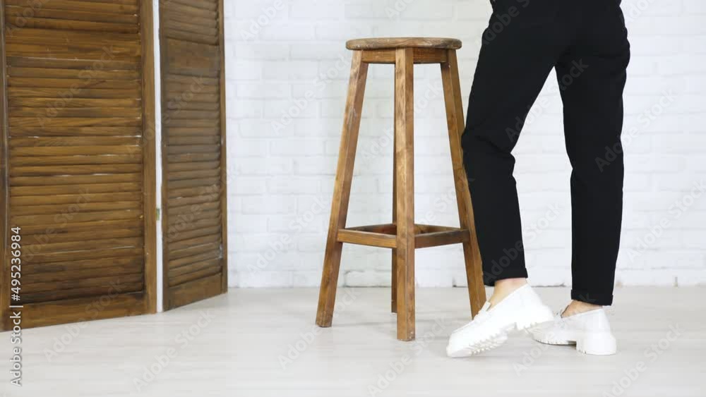 Model in black jeans demonstrating white massive shoes. Lady turns around to show the fashionable footwear. Wooden tabouret at backdrop. Model in black jeans demonstrating white massive shoes. Lady turns around to show the fashionable footwear. Wooden tabouret at backdrop.