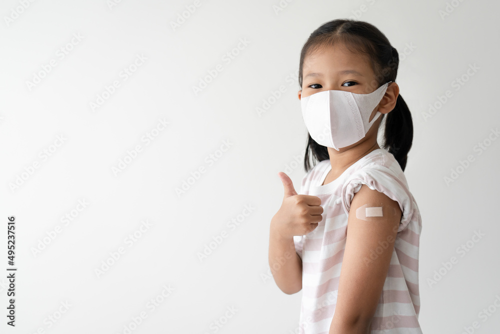 Asian little girl showing her arm with plaster wearing medical mask gesturing thumb up after virus vaccine. Kid and child vaccination campaign Asian little girl showing her arm with plaster wearing medical mask gesturing thumb up after virus vaccine. Kid and child vaccination campaign