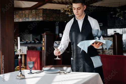 A young male waiter in a stylish uniform is engaged in serving the table in a beautiful gourmet restaurant. A high-level restaurant. Table service in the restaurant.