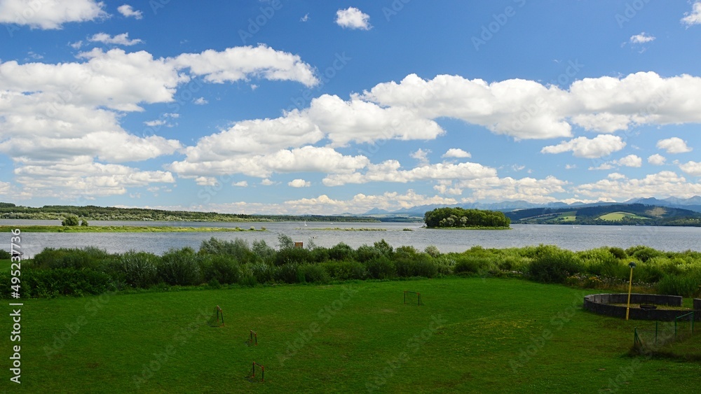 Beautiful summer landscape on Orava river dam, northern Slovakia. Lawn with football goalmouth and shoreline bushes in front, Slanica Island Of Art visible in the center of dam.
