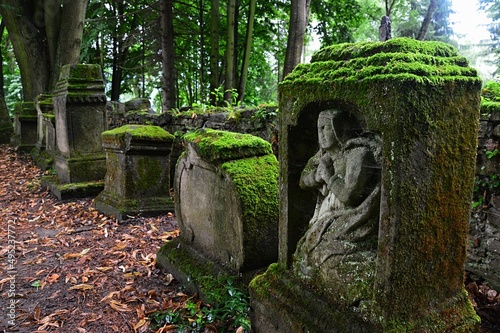 Ancient moss covered remains of cemetery gravestones, one in front with scuplture of praying person, located on church cemetery in Orava region, northern Slovakia. Humid cloudy day photo