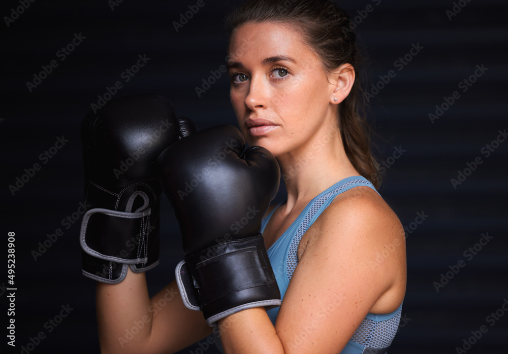Unbreakable and undefeated. Portrait of a young woman wearing boxing gloves against a black background.