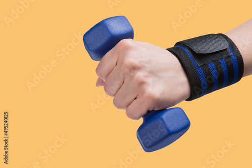 a blue dumbbell in a female hand, a wristband with blue stripes on the wrist, a concept, on a yellow background