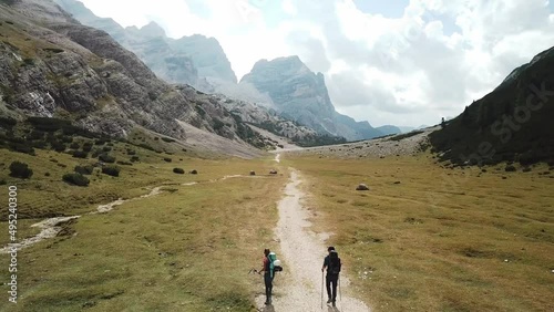 A couple hiking along a gravelled pathway leading through a valley in Italian Dolomites. High, sharp mountains around. Stony and raw landscape. Remote and desolate place. Freedom of exploration
 photo