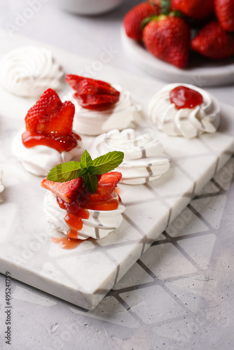 Mini-pavlova with fresh strawberries and red jam - delicious meringue cakes on marble board on off-white background