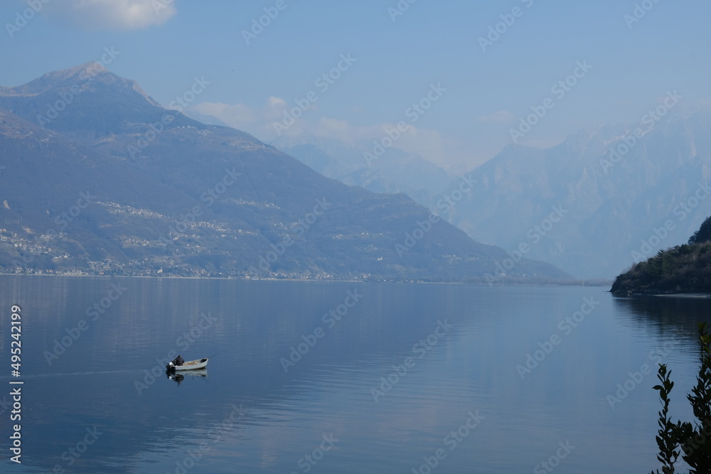 Lonely fisherman on Lake Como, mountains are reflected in the lake. Charon. Avanescent atmosphere. Lonely fisherman on Lake Como, mountains are reflected in the lake. Charon. Avanescent atmosphere.