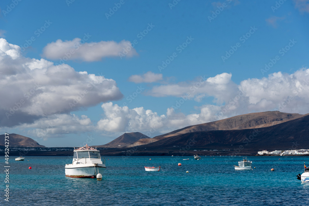 mar azul claro en calma con barcos blancos y montañas volcánicas en la parte trasera de las islas canarias de Lanzarote