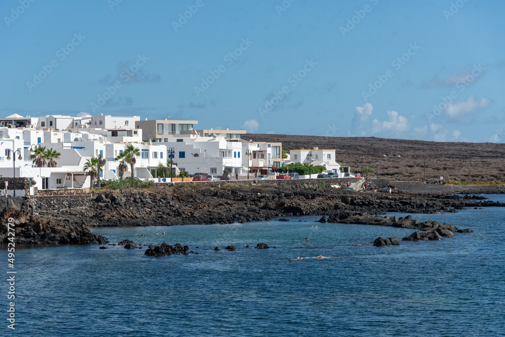 Casas típicas canarias en Punta Mujeres en Lanzarote, Isla Canarias. Paisaje de la costa canaria con marea baja y rocas volcánicas. Verano en la isla con cielo azul. 
