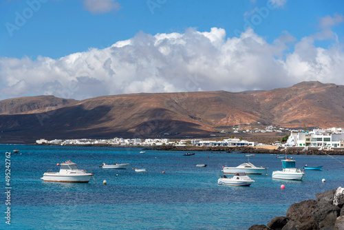 barcos blancos de recreo varados en la costa de Punta Mujeres en Lanzarote, Isla Canarias. Volcanes detrás de casas blancas en canarias. Paisaje turístico con el mar azul turquesa. 