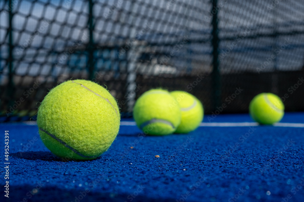 four paddle tennis balls and the net of a blue paddle tennis court, selective focus