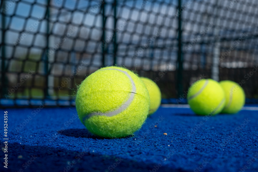 four paddle tennis balls and the net of a blue paddle tennis court, selective focus