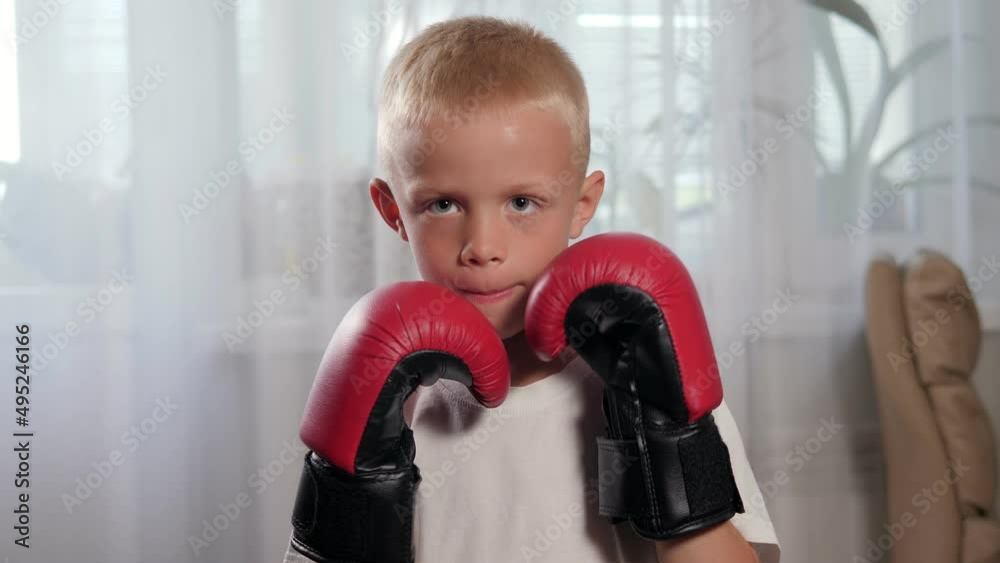 A small seven-year-old boy in boxing gloves practices punches at home. Children's sports. A small seven-year-old boy in boxing gloves practices punches at home. Children's sports.