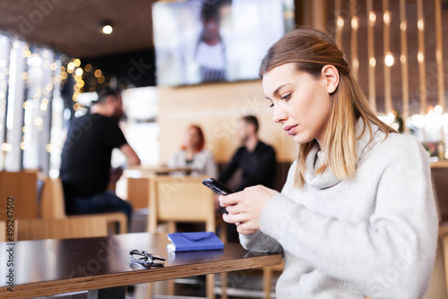 Girl at a modern cafe looking at phone. Smiling.