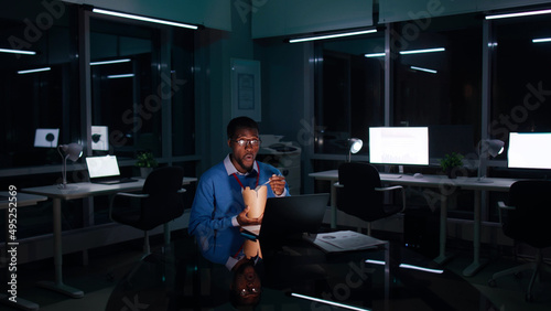 African-American businessman work late in dark office and eat takeaway food