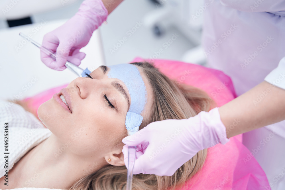 Beautician applying mask to patient face with brushes Beautician applying mask to patient face with brushes