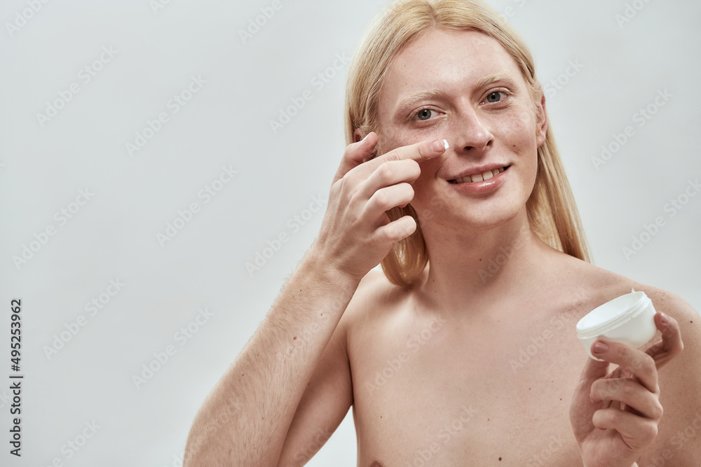 Guy smearing cosmetic cream from container on face Guy smearing cosmetic cream from container on face