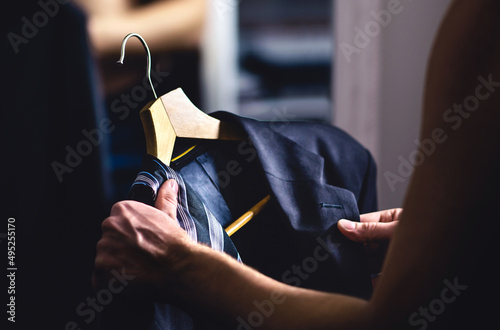 Man getting ready and dressing up in a suit. Luxury jacket and tie in hanger. Trying on outfit before date or wedding. Fitting room in mall store, closet or tailor shop. Formal businessman fashion. photo